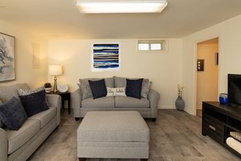A living room with a grey couch, a grey ottoman, and a painting on the wall.